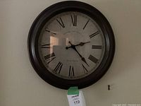 Photo of the 15-inch round Edinburgh Clock Works Co. wall clock mounted on a wall with a dark frame and Roman numeral dial.