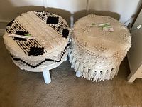 Two round foot stools side by side with distinct macrame covers, one black and cream and one cream tufted.