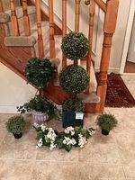 Full view of all 5 pieces of artificial greenery arranged on floor near stairway showcasing variations in shape and pot style.