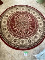 Top view of 5 ft round red and beige area rug with ornate central medallion design on tile floor.