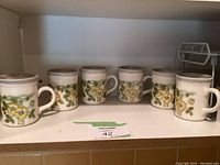 Six Biltons floral ceramic mugs arranged in a row on a shelf, showing front sides and handles.
