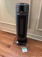 Full view of the Delonghi ceramic fan heater standing on wooden floor showing its tower design and front grill.