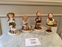 Four figurines displayed on table: a shepherd boy with lambs, a girl knitting, a boy with a staff, and a girl with a basket.