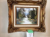 Full view of the ornate gold framed landscape painting showing river, trees, and mountains