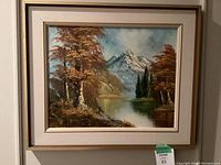 Framed scenic painting mounted on a wall, showing mountain peak, lake, and fall trees.