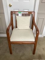 Front view of wooden occasional chair with cream seat cushion and back pillow placed against a white door.