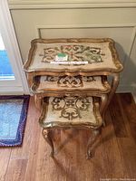 Top-down view of all 3 tables stacked, showing the decorative painted tops with wear, scalloped edges and curved legs.