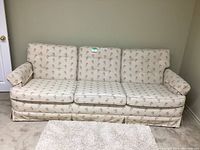 Front view of three-seat sofa showing floral upholstery, removable cushions, and skirted base.