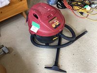 Full view of the Shop-Vac wet/dry vacuum with attached hose and nozzle, showing the unit's red top and black bottom with handle and hose.