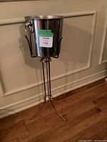 Front view of the stainless steel wine/champagne bucket on its metal stand, showing the ring handles and the stand's leg structure.