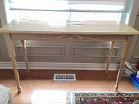Front view of the wood sofa table showing turned legs, decorative carving on apron, and light wood finish.