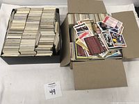 Two boxes shown with large quantities of baseball cards; one box neatly packed with cards and the other box loosely filled with loose and scattered cards on top.