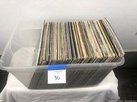 Clear plastic tub filled with standing, used vinyl records as seen from top angle showing many records packed inside the tub.