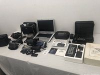 Overall view of assorted electronics including laptop, cameras, calculator, headphones, and carrying cases.