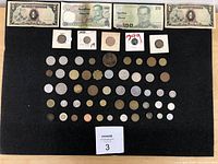 Top-down view of the full lot arranged on black surface showing three foreign banknotes and many coins in multiple rows and columns, with visible wear on some coins and notes.