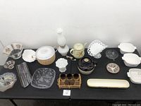 Overview of assorted ceramic and glass dishes and decorative items arranged on black table.