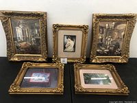 Group of five thick gold ornate framed photo prints shown on black surface.