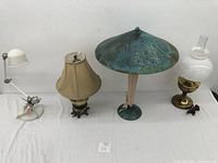 Group of 4 lamps including metal dome shade lamp, beige fabric shade lamp, modern swivel white lamp, and white glass hurricane shade lamp