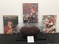Overview of Joe Montana autographed football in case with three magazines behind