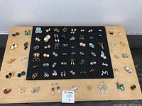 Full lot of 73 pairs of various costume women's earrings laid out on black felt and wooden surface.