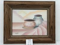 Front view of framed oil painting showing two Native pottery vessels, mountain background, signed by artist.