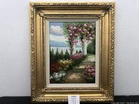 Full view of the framed oil painting showing the garden pathway scene with pink flowering trees and a blue sky.