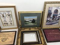 Six framed artworks including floral urns, landscape, city street, vintage port labels, and empty frame.