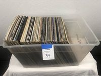 Side view of clear plastic tub filled with numerous vinyl records.
