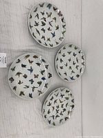 Four round white porcelain plates decorated with a wide array of colorful butterflies in flight patterns, arranged side by side and overlapping slightly.