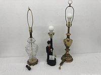 All three lamp stands together showing brass, brass and glass, and Charlie Chaplin figurine lamps.