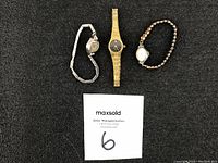 Photo showing three vintage women's wristwatches (Elgin, Waltham, Benrus) laid out on black background with MaxSold auction label.