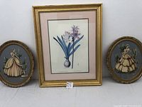 Overall view of three framed wall art pieces including botanical print center and two oval portraits on sides