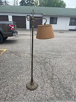 Full view of the tall metal bridge floor lamp with brown fabric shade standing on asphalt.