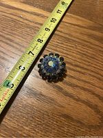 Photo of the brooch with a measuring tape showing size of about 1.5 inches diameter, highlighting stone arrangement.