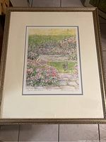 Framed print showing garden scene with cat, flowers, and path, with mat and frame visible