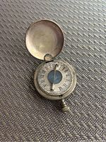Open view of antique pocket compass with sundial showing Roman numeral hour markers and central compass needle.