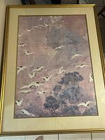 Framed print depicting white cranes flying over trees and mountains in muted tones