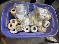 Plastic tub filled with several spools and balls of white crochet yarn, some in plastic bags.