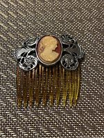 Front view of the hair clip showing the detailed cameo and silver-toned filigree base attached to the golden comb teeth.