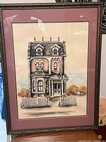 Framed Victorian style house in ink and watercolor with ornate roof, bay windows, picket fence, and autumnal background trees.