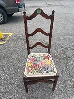 Full view of the wooden ladder back chair with needlepoint floral cushion on the seat, shown outdoors on pavement.