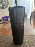 Front view of the matte black Starbucks venti cup with embossed logo and black straw on a dining table.