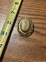 Full view of brooch next to measuring tape showing size about 1.5 inches long.