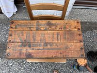 Top view of a rectangular wooden box lid with the word 'SALADS' faintly visible, showing aged and worn wood surface.