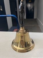 Front view of a brass school hand bell with a black wooden handle, showing the condition and materials.