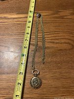 Full view of gold-tone slide chain necklace with photo pendant next to measuring tape showing length approximately 12 inches.