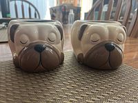 Two small ceramic puppy face planters displayed side by side on a table, showing front facial details.