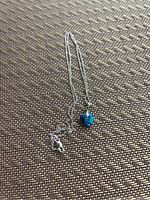 Photo of a delicate sterling silver chain with a small blue crystal heart pendant placed on a woven textured surface.