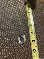 Sterling silver necklace with thin chain and square pendant featuring circular cut-out and green stone accent.
