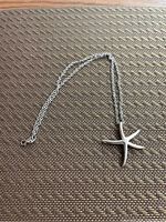 Photo showing the sterling silver necklace laid out with the starfish pendant in the center on a textured surface.